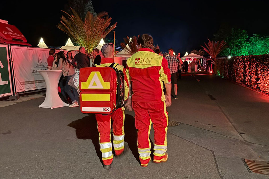 2 Sanidiensthelfer stehen mit dem Rücken zu uns und beobachten die Menge bei einem Fußballspiel. 