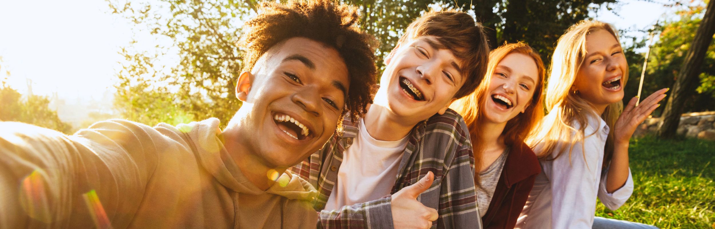 4 jungen Menschen sitzen nebeneinander und lachen herzlich in die Kamera