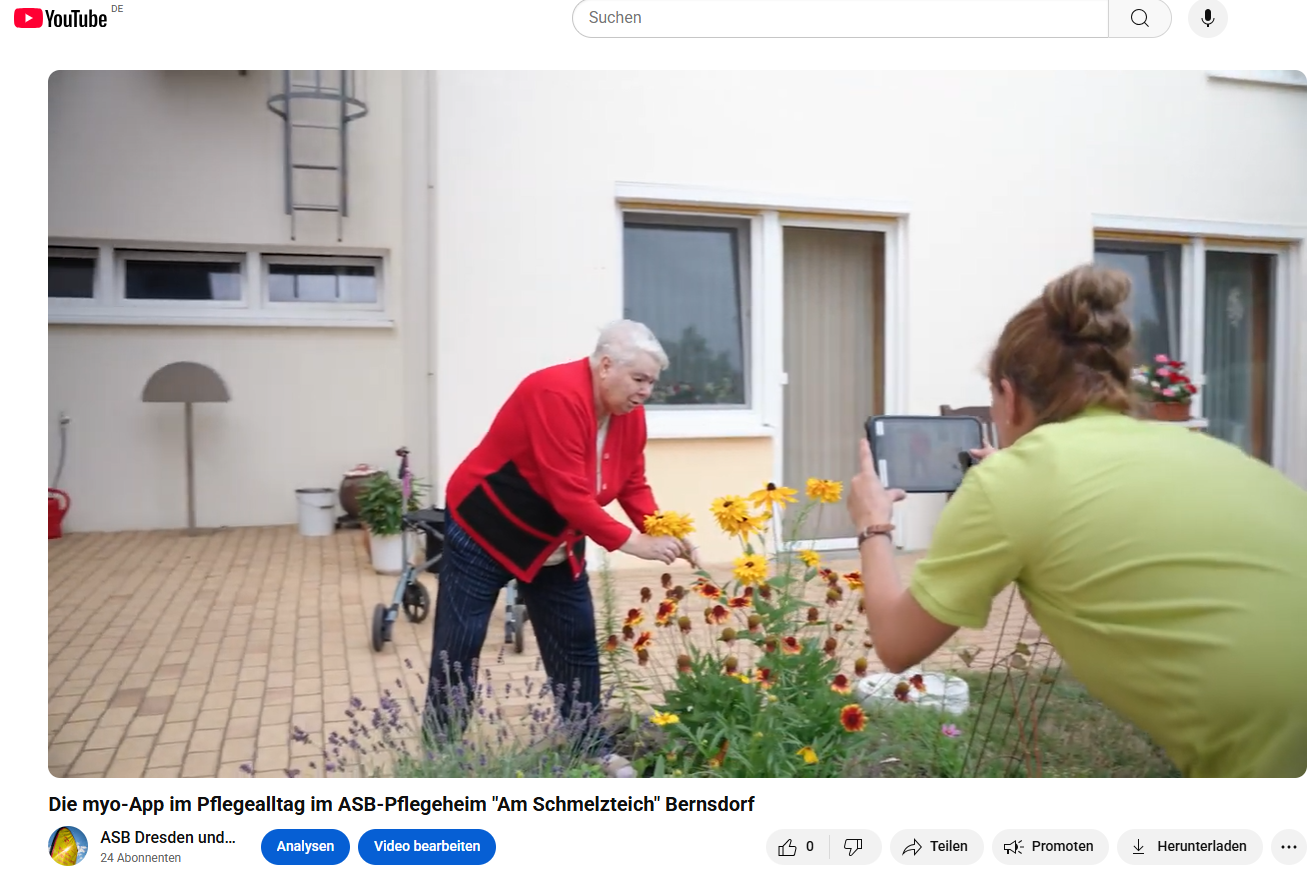 Eine Bewohnerin erfreut sich an Blumen während die Betreuerin ein Foto davon macht. 