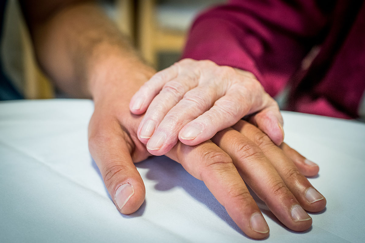 Hände eines älteren Menschen und eines Pflegers, die sich berühren