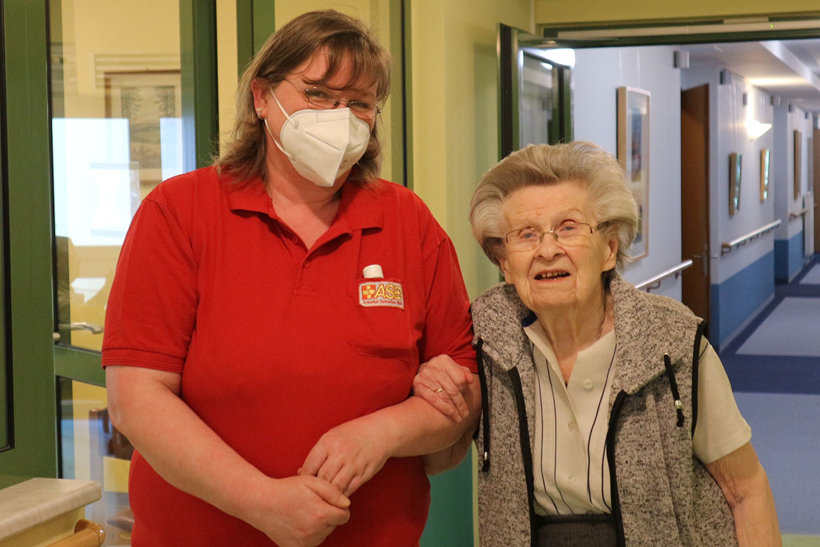 Pflegehilfskraft Antje Schreivogel begleitet eine Bewohnerin auf dem Gang.