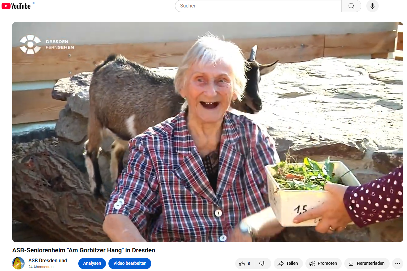 Eine Bewohnerin sitz während der Fütterung der Ziegen mit im Gehege und hilft.